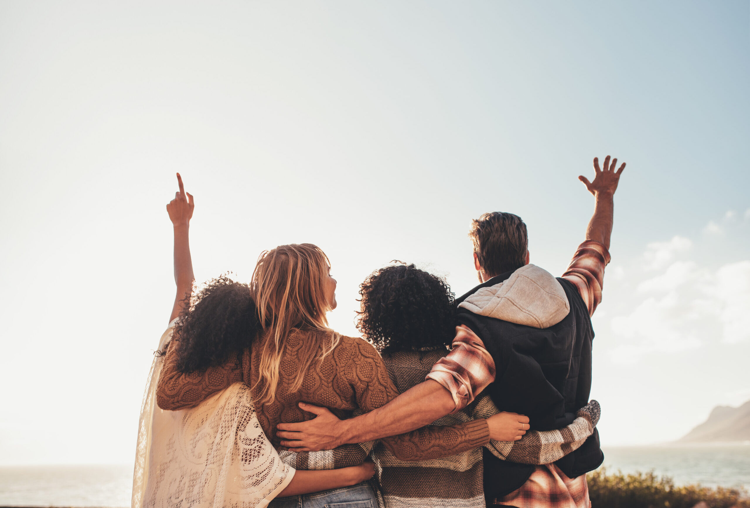 Four friends standing together with their arms raised. Group of man and women enjoying on vacation.